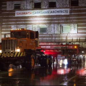 Nighttime image of a large truck transporting a log cabin.