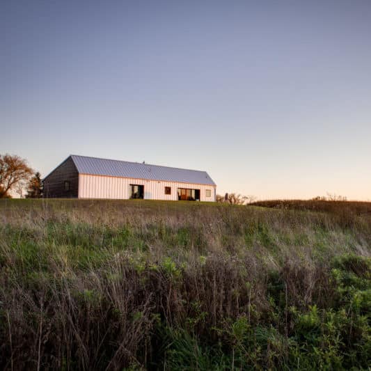 A rustic farm shed set upon a slight grassy hill in sunset.